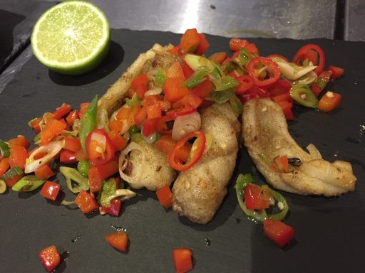 Grilled fish garnished with fresh salsa and a lime wedge.