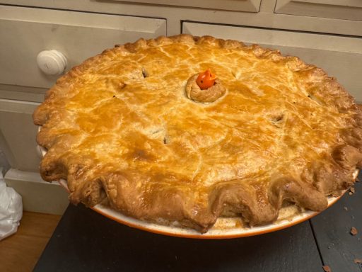 Golden-brown pie with a decorative top and a small red garnish in the centre.